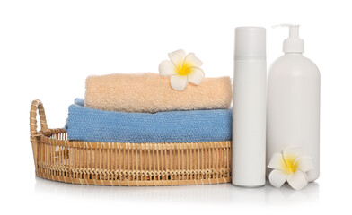 Obraz na płótnie Canvas Soft towels in wicker basket, bottles of cosmetic products and plumeria flowers on white background