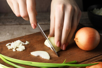 Woman cutting ripe onion at wooden table, closeup