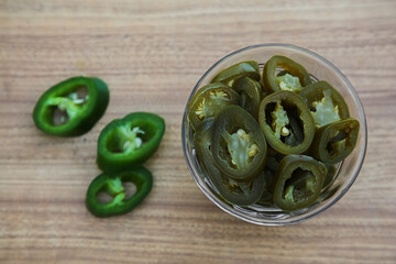 Fresh and pickled green jalapeno peppers on wooden table, flat lay