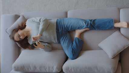 Young lady lying on the couch, holding a smartphone, using an app