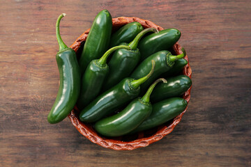 Bowl with green jalapeno peppers on wooden table, top view