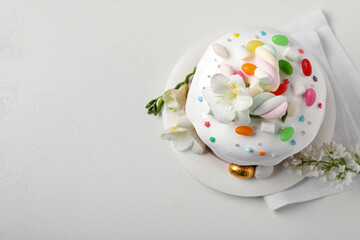 Traditional Easter cake with sprinkles, jelly beans, marshmallows and decorated eggs on white table, flat lay. Space for text