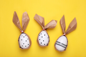 Easter bunnies made of craft paper and eggs on yellow background, flat lay