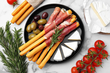 Delicious grissini sticks with prosciutto and ingredients on white marble table, flat lay