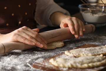Woman rolling dough for chebureki at wooden table, closeup