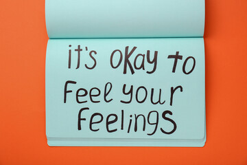Notebook with phrase It`s Okay To Feel Your Feelings on orange background, top view