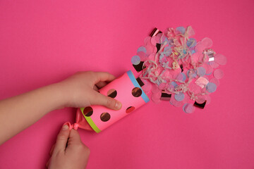 Woman holding party popper with serpentine and confetti on pink background, top view