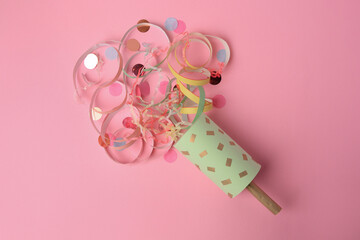 Beautiful serpentine and confetti bursting out of party popper on pink background, flat lay