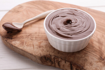 Bowl with tasty chocolate paste and spoon on white wooden table, closeup. Space for text