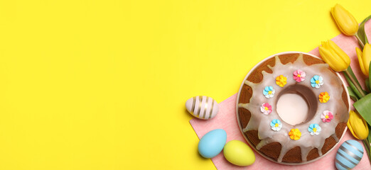 Delicious Easter cake decorated with sprinkles, beautiful tulips and painted eggs on yellow background, flat lay. . Banner design with space for text