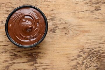 Bowl of chocolate paste on wooden table, top view. Space for text