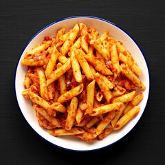 Homemade Penne With Tomato Sauce on a Plate on a black background, top view.
