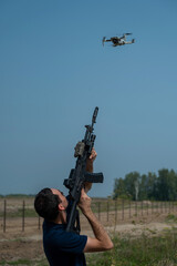 Man aiming to shoot a rifle at a flying drone outdoors. 