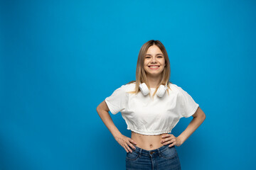 Beautiful young blonde woman with headphones and mobile device listening to music and smiling and dancing, isolated on blue background.