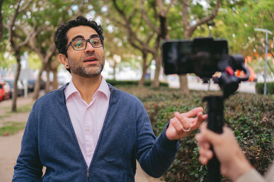 Middle-aged man doing a video blog in a green area of the city while being recorded with a cell phone on a gimbal.