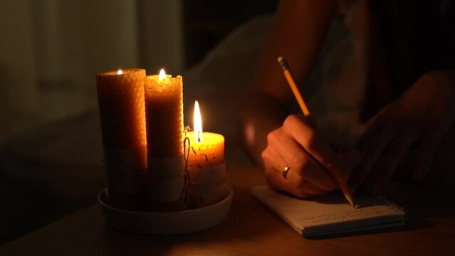 A woman makes notes in a notebook in a dark room with burning candles. Close-up. Magic and occultism.