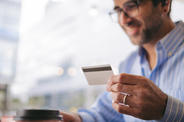 Smiling middle-aged latin blurred man using a credit card in a coffee shop. Copy space.