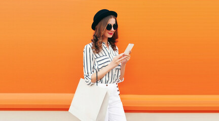 Portrait of beautiful young woman looking at smartphone with shopping bag wearing white striped...