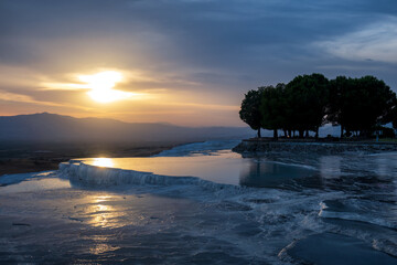 Beautiful Pamukkale in Turkey. Colorful  sunrise and reflection from natural travertine pools. Silhouettes of mountains in the background.