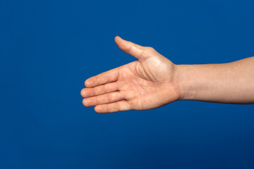 Man stretching out his hand to handshake isolated on a blue background. Man's hand ready for handshake. Formal greeting, gesture of introduction and respect towards someone.