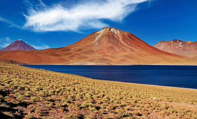 Awesome wild desert landscape, dark blue lake, red volcano Miniques peaks, sandy area with dry...