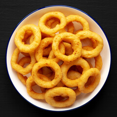 Homemade Breaded Onion Rings on a Plate on a black background, top view. Flat lay, overhead, from above.