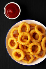Homemade Breaded Onion Rings with Ketchup on a Plate on a black background, top view. Flat lay, overhead, from above. Close-up.