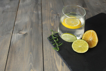 water with lemon homemade lemonade in a glass next to there are lemons with herb green rosemary on a black stand with a place for text. Healthy food drink drinks
