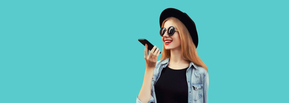 Portrait of happy smiling young woman with smartphone using voice command recorder, assistant or takes calling isolated on blue background, copy space