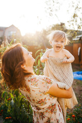 A young woman holds her little son in her arms in the garden at sunset