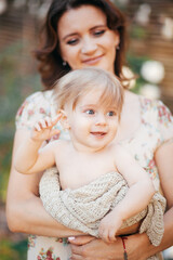 A young woman holds her little son in her arms in the garden at sunset