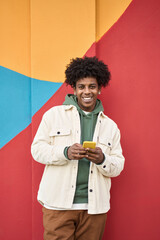 Happy smiling young African American hipster gen z guy standing at color bright red wall outdoors...
