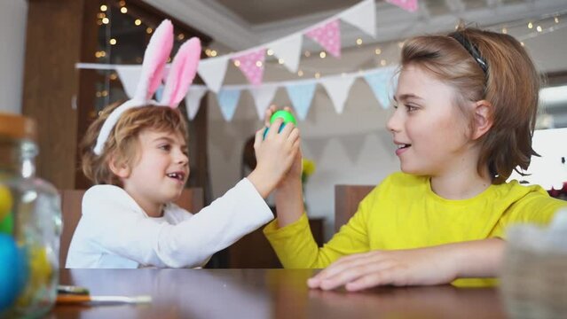 Easter Sunday Family holiday traditions. Two caucasian happy siblings kids with bunny ears fighting with multi-colored Easter painted eggs. Having fun together