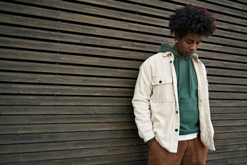 Cool hipster young African American stylish rebel vulnerable guy standing at city wooden wall....