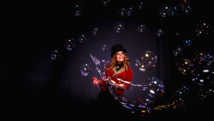Magician lady make soap bubbles show, an illusionist in theatrical clothes posing at black...