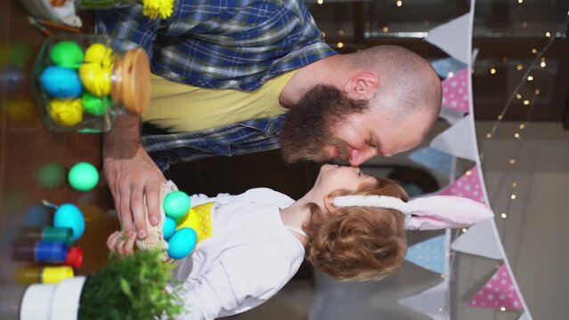 Easter Family traditions. Dad and preschool happy child daughter with bunny ears playing and paint with Easter decorated eggs together at Easter sunday holiday. Cosy embrace Vertical