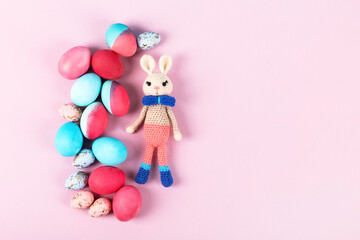 Painted Easter eggs in crimson and blue with crocheted easter bunny on a pink background with a place for text. Happy Easter concept. Greeting card, copy space