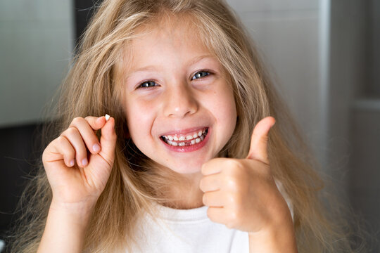 a little blonde girl in the bathroom looks into the camera, smiles and shows a fallen milk tooth, close-up