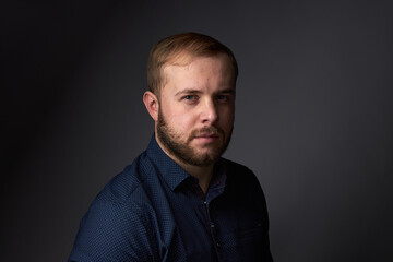 Fototapeta premium Portrait of a young confident blonde in a dark shirt, with a beard on a dark background