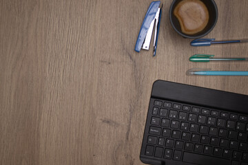 tablet keyboard and stapler colored pens and a gray coffee mug a wooden table with space for text 