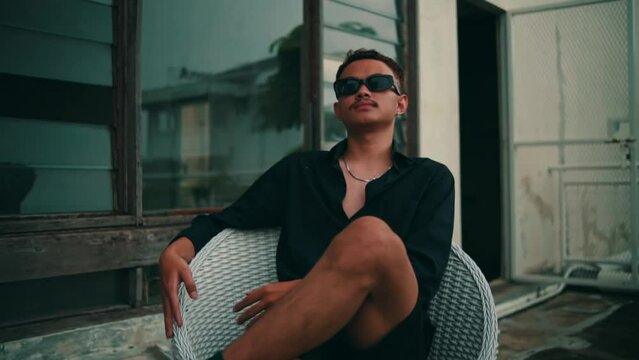 Portrait of a young Asian man with sunglasses sitting in a chair outdoors while looking at the camera