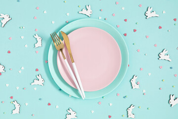 Easter holiday composition.Top view of pink plate with knife and fork and  wooden toy rabbit, sugar...