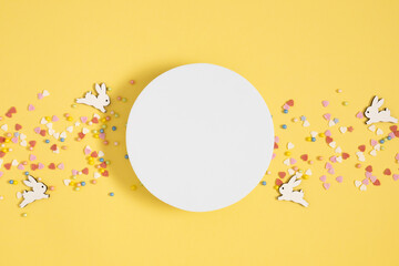 Easter holiday composition. Easter decorations empty round platform podium, feathers and rabbit toy isolated on pastel yellow background. Easter concept. Flat lay, top view, copy space