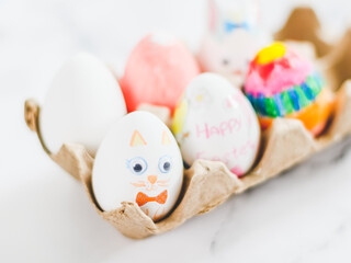 Cardboard package with decorated Easter eggs with glued and painted Easter bunny faces on a marble...