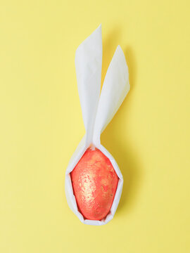 A do-it-yourself decorative orange marble egg with white paper ears on a yellow background.