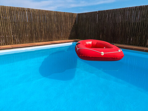 Red inflatable boat floating in a private swimming pool, no people.