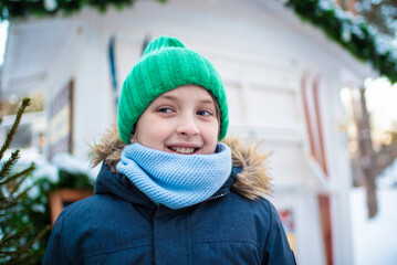 miling boy with green cap in snowy winter at fair, festival	