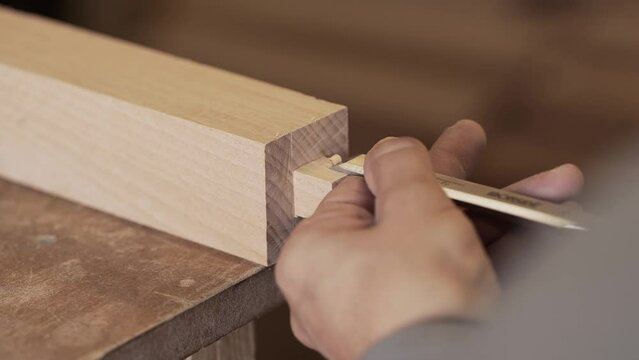 Close-up of a carpenter working on beech wood, with a chisel he carves the wood making a tenon to assemble