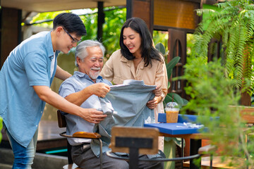 Asian couple surprised elderly father with Birthday gift at outdoor cafe restaurant on summer holiday vacation. Family relationship, celebrating father's day and older people health care concept.