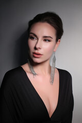 Portrait of a beautiful fashionista brunette girl, with long silver earrings, in black with a...